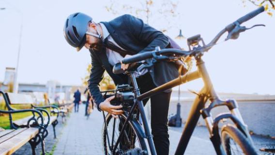 Un homme portant un casque de vélo enlève sa batterie de bicyclette électrique.