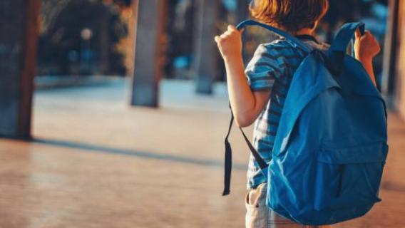 Un enfant marche avec un cartable bleu sur les épaules.