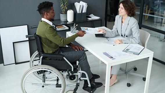 Une personne en fauteuil roulant discute avec un recruteur autour d'un bureau