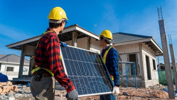 Deux ouvriers en tenue et casque de chantier d&eacute;placent un panneau solaire.