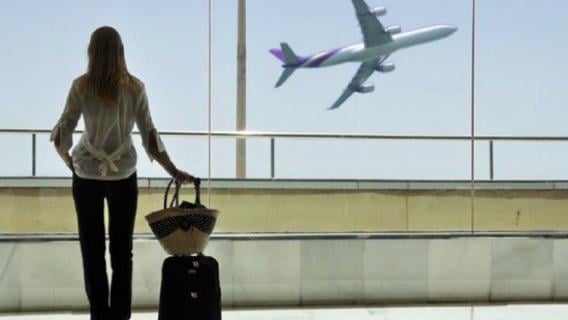 Dans un aéroport, une femme de dos regarde un avion décoller