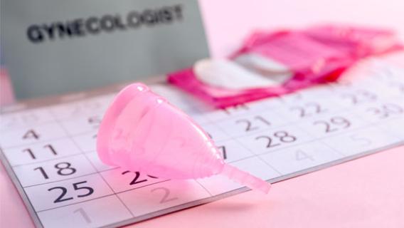 Une coupe menstruelle rose est posée sur un calendrier.