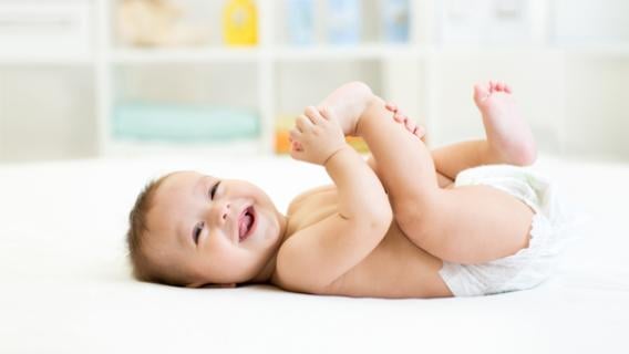 Un bébé vêtu d'une couche blanche est posé sur le dos et joue avec ses pieds