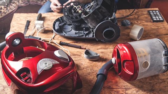 Un aspirateur filaire rouge a &eacute;t&eacute; d&eacute;mont&eacute; afin de le r&eacute;parer, toutes les pi&egrave;ces sont pos&eacute;es sur une table