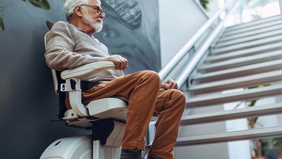 Un homme aux cheveux blancs utilise un monte-escalier pour gravir les marches le menant au premier &eacute;tage de son logement