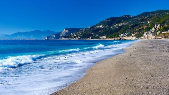 Un paysage de plage bordée d'une mer bleue avec en fond un village.