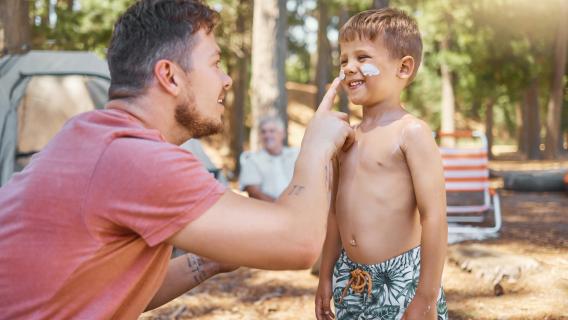 Un homme mettant de la cr&egrave;me solaire &agrave; son enfant/ camping en for&ecirc;t