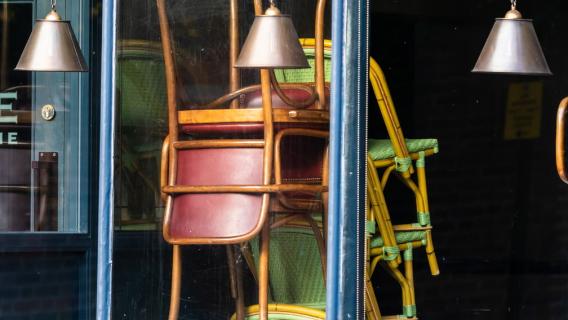Des chaises empilées derrière la vitre d'un établissement, visiblement fermé