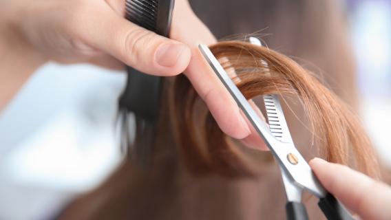 Des mains qui tiennent une mèche de cheveux dans une paire de ciseaux