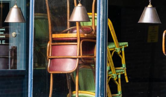 Des chaises empilées derrière la vitre d'un établissement, visiblement fermé
