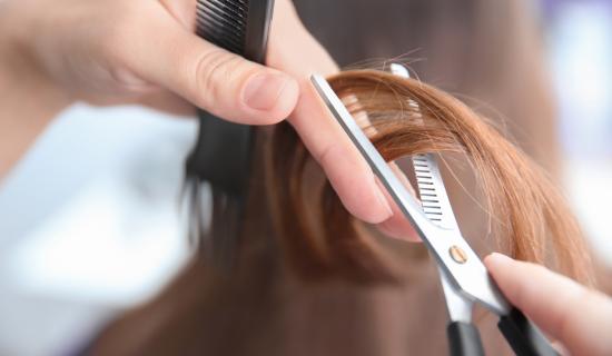 Des mains qui tiennent une mèche de cheveux dans une paire de ciseaux